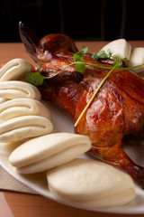 A view of a platter of Peking Duck, with several bao rolls, in a restaurant or kitchen setting.