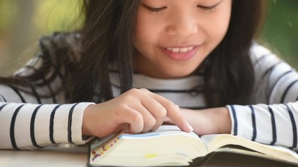 Wall Mural - cute little asian girl in reading bible. hands holding on a holy bible. little child girl hands folded in prayer on a holy Bible for faith,spirituality and religion concept.