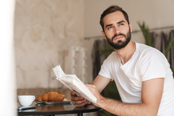 Wall Mural - Man indoors at home have a breakfast reading book.