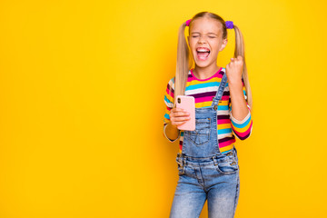 Wall Mural - Portrait of delighted kid use cellphone win social network lottery raise fists scream yeah wear striped sweater jumper denim jeans isolated over shine yellow color background