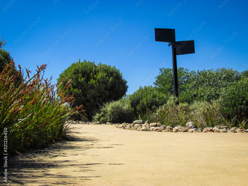 Footpath at a public park with signage pole surrounded by garden plants ...