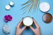 Woman's hands holding jar with cream over blue table with cosmetic products 