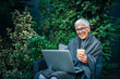 © bnenin - Portrait of a cheerful modern elderly woman using laptop in the garden.