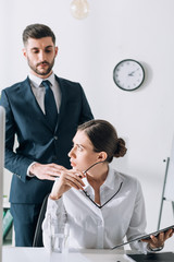 Wall Mural - handsome businessman in suit touching shocked businesswoman in office