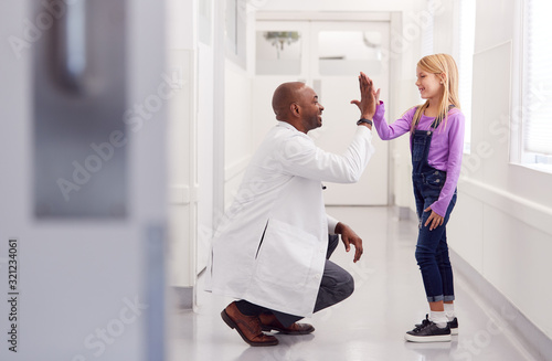 Cuadros en Lienzo Male Paediatric Doctor Giving Young Girl Patient High Five In Hospital Corridor