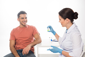 Wall Mural - Smiling doctor showing vaccine to patient isolated on white