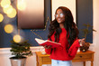 Happy african american woman in a red jumper stands with a book in hand. Young girl in home christmas interior.