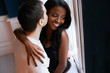 Happy, loving young interracial couple cuddling while standing near the window. Beautiful black girl smiles while kissing.