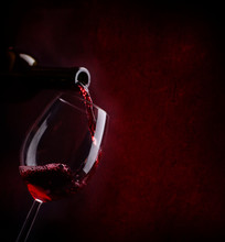 Red Wine Pouring In Wineglass From Bottle Over Dark Background.