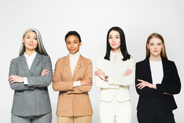 Wall Mural - multicultural businesswomen in suits standing with crossed arms isolated on white