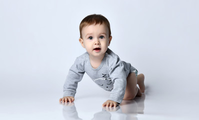 little baby boy toddler in grey casual jumpsuit and barefoot crawling on floor, smiling and looking 