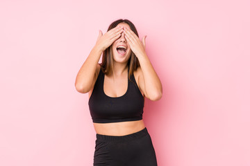 Wall Mural - Young fitness caucasian woman isolated covers eyes with hands, smiles broadly waiting for a surprise.