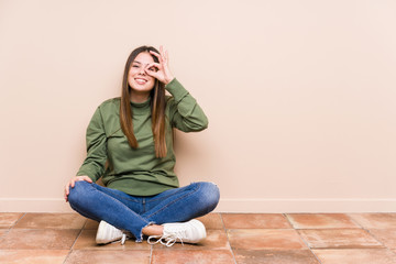 Wall Mural - Young caucasian woman sitting on the floor isolated excited keeping ok gesture on eye.