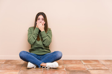 Wall Mural - Young caucasian woman sitting on the floor isolated shocked covering mouth with hands.