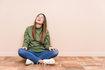 Wall Mural - Young caucasian woman sitting on the floor isolated relaxed and happy laughing, neck stretched showing teeth.