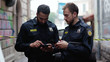 © Fractal Pictures - Police at raid. Close-up two handsome policemen searching on smartphones tracking a criminal online. Friendly colleagues cops at police investigation area in the city street.