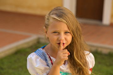 Shh, hush, my mom is sleeping. Frustrated little girl shows silence gesture with hand finger to her mouth isolated outside external house wall on background