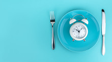 Alarm Clock With Fork And Knife On The Table. Time To Eat, Breakfast, Lunch Time And Dinner Concept