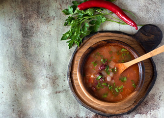 Spicy tomato soup with beans on a wooden plate on a gray background