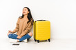 © Asier - Young chinese traveler woman sittting on the floor with a suitcase isolated relaxed and happy laughing, neck stretched showing teeth.