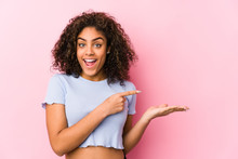 Young African American Woman Against A Pink Background Excited Holding A Copy Space On Palm.