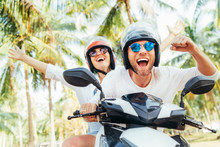 Happy Smiling Couple Travelers Riding Motorbike Scooter In Safety Helmets During Tropical Vacation Under Palm Trees On Ko Samui Island In Thailand