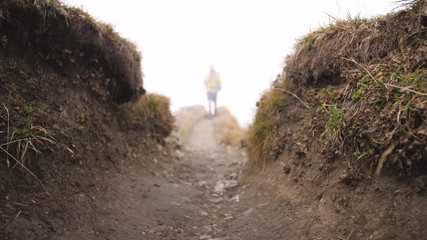 Wall Mural - young man hiker on mountain with cloudy sky and fog. yellow jacket, backpack and beanie. traveling d