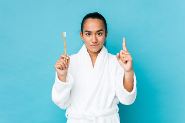 Young mixed race indian holding a toothbrush showing number one with finger.