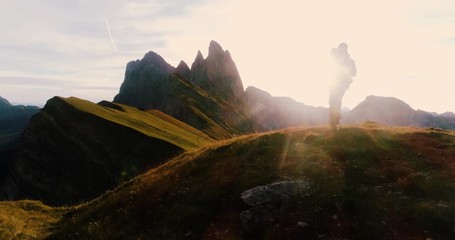 Wall Mural - aerial view. young man hiking at seceda mountain arriving to peak at sunrise. backpack, yellow jacke