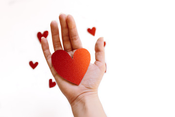 Red glitter heart shaped cardboard on the hand and small hearts on white background. Concept of love and valentines day.