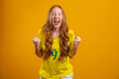 © Nexa - Brazil supporter. Brazilian redhead woman fan celebrating on soccer, football match on yellow background. Brazil colors.