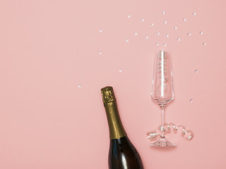 A bottle of sparkling wine and a glass with streamers and stars on a pink background.