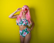 © Михаил Решетников - Beautiful girl in a pink wig and colored bikini posing on a yellow background. Woman with artificial long hair and pink glasses in the form of hearts.