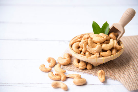 roasted salted raw cashew nuts with fresh cashew in spoon and basket isolated on white wooden backgr