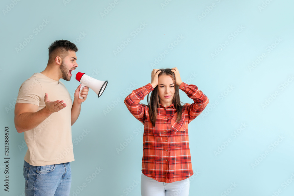 Angry man with megaphone shouting at his wife on color background