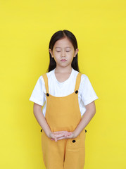 Peaceful asian little girl with closed eyes standing isolated on yellow background. Kid in meditation expression