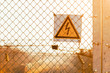 Yellow high voltage warning sign on an iron mesh fence over railroad tracks at sunset with copy space.
