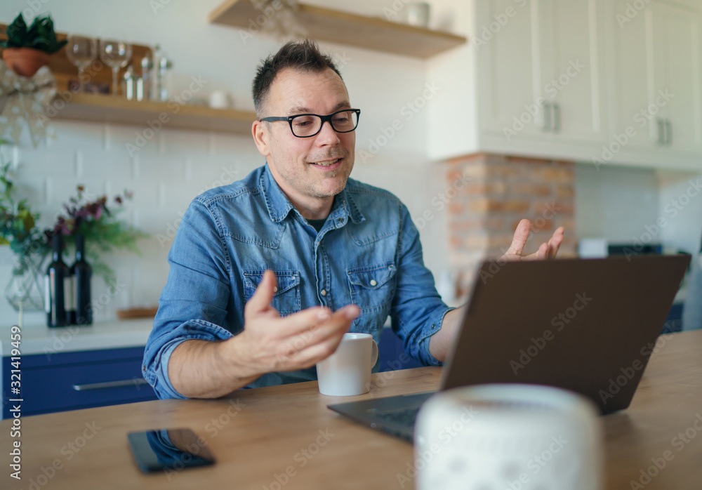 Happy adult man having a video call with a laptop at home - obrazy, fototapety, plakaty 