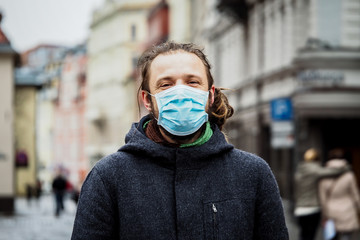 Handsome young European man in winter clothes on the street with a medical face mask on. Closeup of a 35-year-old male in a respirator to protect against infection with influenza virus or coronavirus