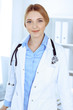 © rogerphoto - Young woman doctor at work in hospital looking at camera. Blue colored blouse of therapist looks good. Medicine and healthcare concept