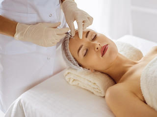 Beautiful woman receiving beauty injections with closed eyes. Beautician doctor hands doing beauty procedure to female face with syringe. Cosmetic medicine and surgery concept