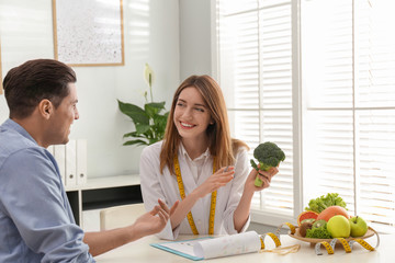 Poster - Young nutritionist consulting patient at table in clinic