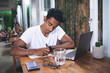 Focused Hispanic man taking notes while working on laptop in cafe