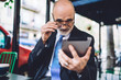 © BullRun - Elderly bearded businessman correcting glasses and working on tablet
