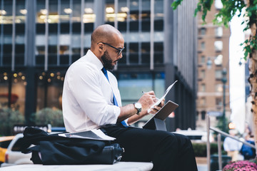 Wall Mural - Black manager with tablet writing on paper on urban bench