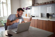 © luckybusiness - adult young man with beard wearing glasses,  watching his cell phone, smiling  in front of laptop on table.  lifestyle, modern, concept
