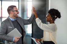 Businessman And Businesswoman Celebrating Success By Doing The High-five In Office Hall. Two Business People High-five. Job Well Done. Two Excited Business Colleagues Team Give High Five