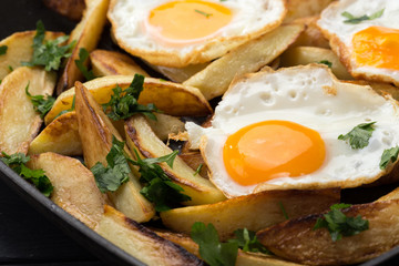 Breakfast in the pan. Fried potatoes with eggs in a skillet. Food bachelor. Cooked by a man. Hot and fresh. Homemade breakfast on black table. Fried eggs and sweet potato hash in cast iron skillet Fre