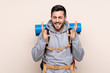 © luismolinero - Young mountaineer man with a big backpack over isolated background laughing
