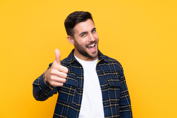 young handsome man with beard over isolated yellow background with thumbs up because something good 